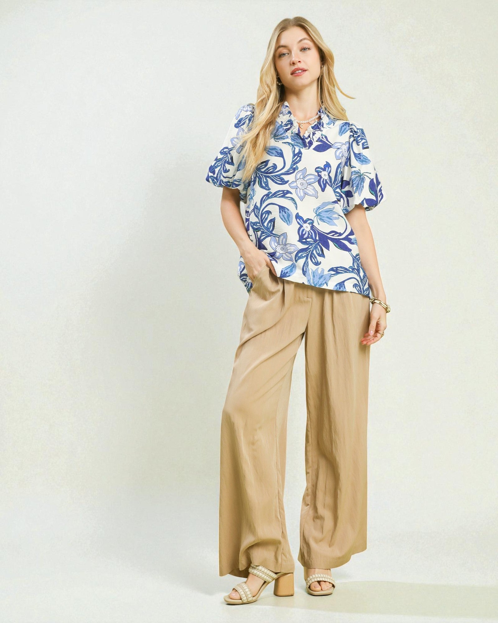 Woman wearing a blue floral blouse and beige pants on a white background