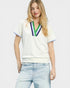 Woman wearing a white blouse with colorful accents and light blue jeans on a plain background