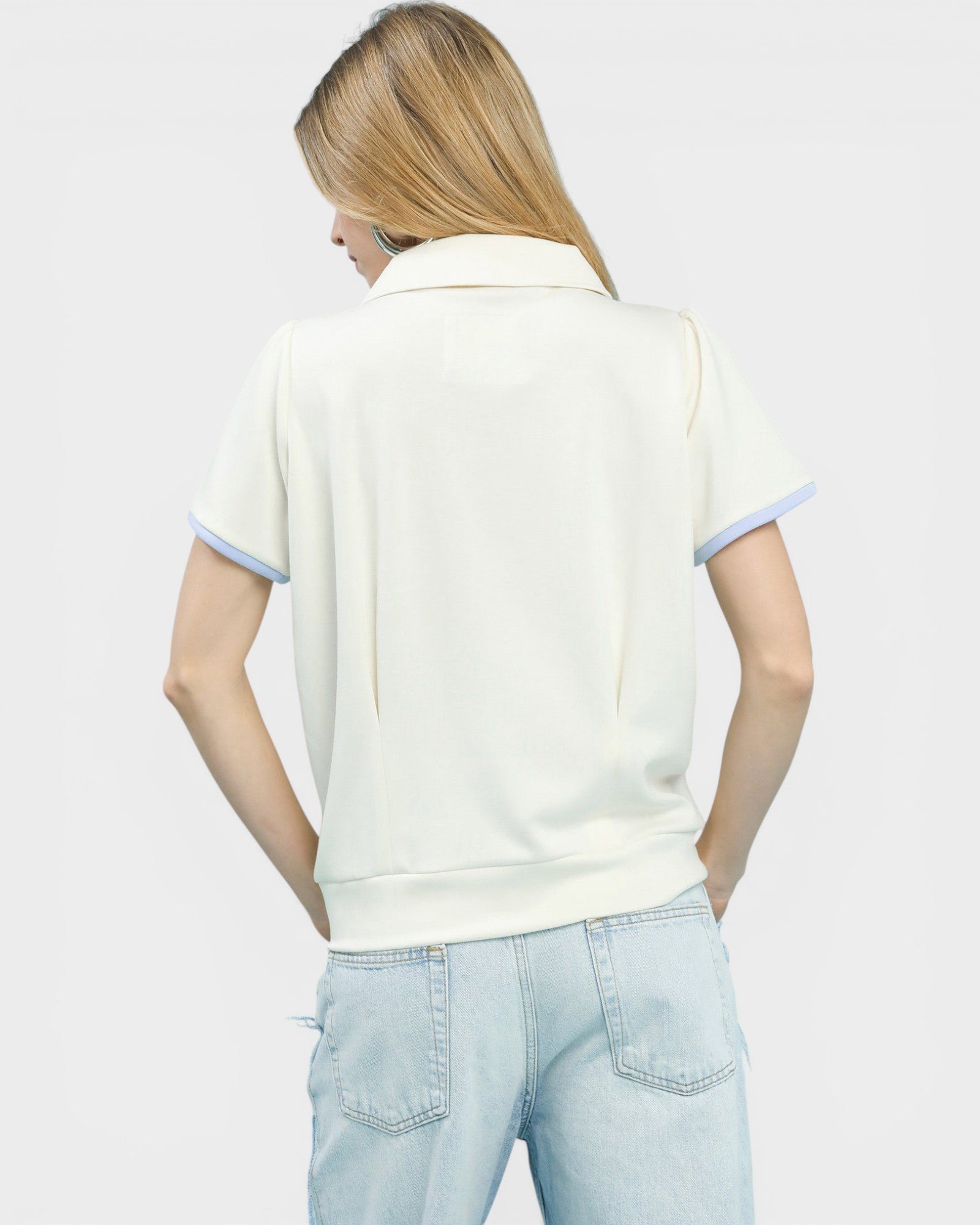 Woman wearing a white polo shirt with light blue trim on a plain background