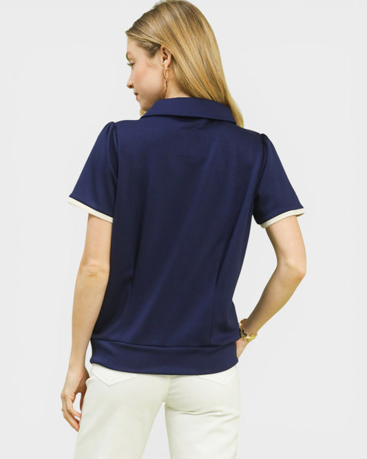 Woman wearing a navy blue polo shirt with white trim on a light gray background