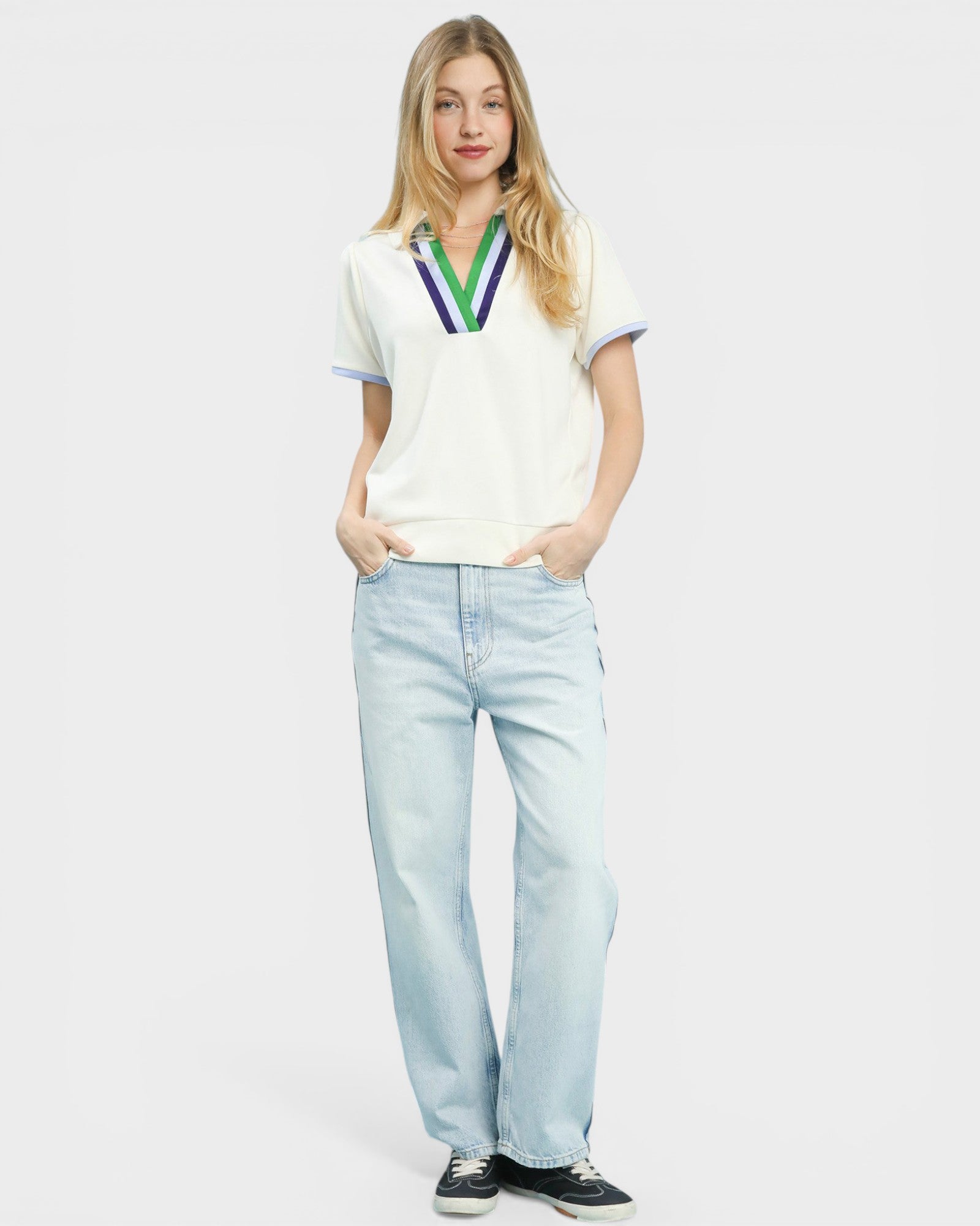 Woman wearing a white polo shirt with colorful accents and light blue jeans on a plain background
