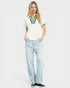 Woman wearing a white polo shirt with colorful accents and light blue jeans on a plain background