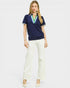 Woman wearing a navy blue polo shirt with a colorful collar and white pants on a light gray background
