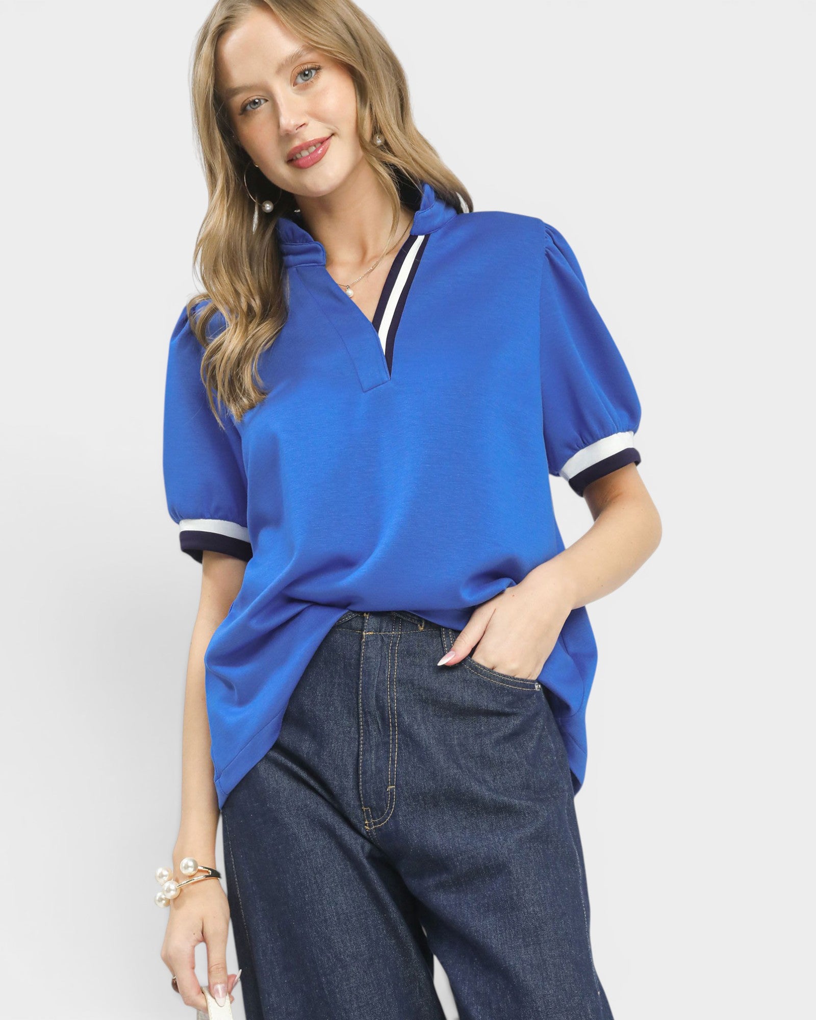 Woman wearing a blue polo shirt with white trim on a plain background