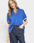 Woman wearing a blue polo shirt with white trim on a plain background