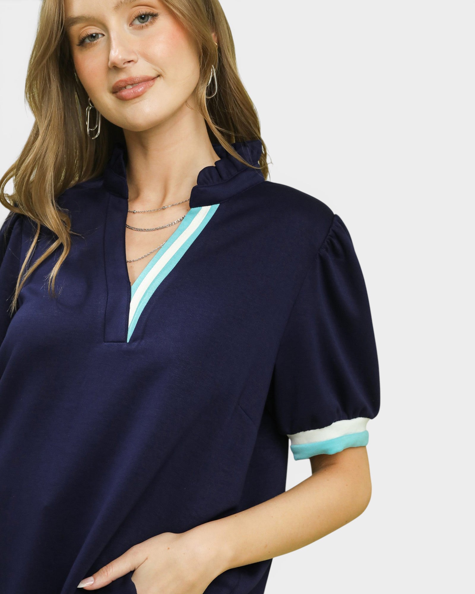 Woman wearing a navy blue top with white and light blue trim on a plain background