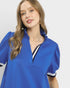 Woman wearing a blue top with white accents on a plain background