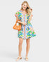 Woman wearing a colorful floral dress holding an orange handbag on a white background