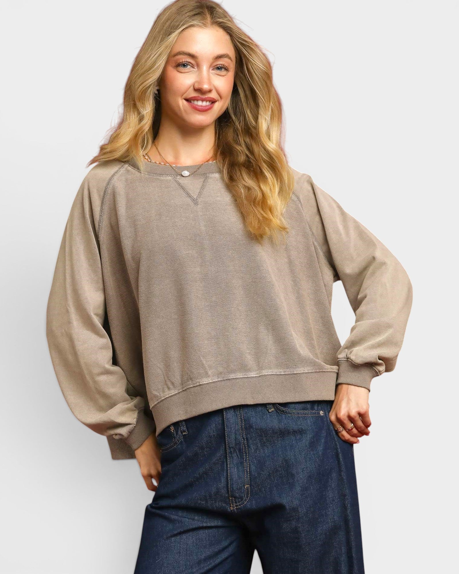 Woman wearing a beige sweater and blue jeans against a white background