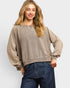 Woman wearing a beige sweater and blue jeans against a white background