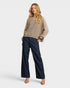 Woman wearing a beige sweater and dark blue jeans on a white background