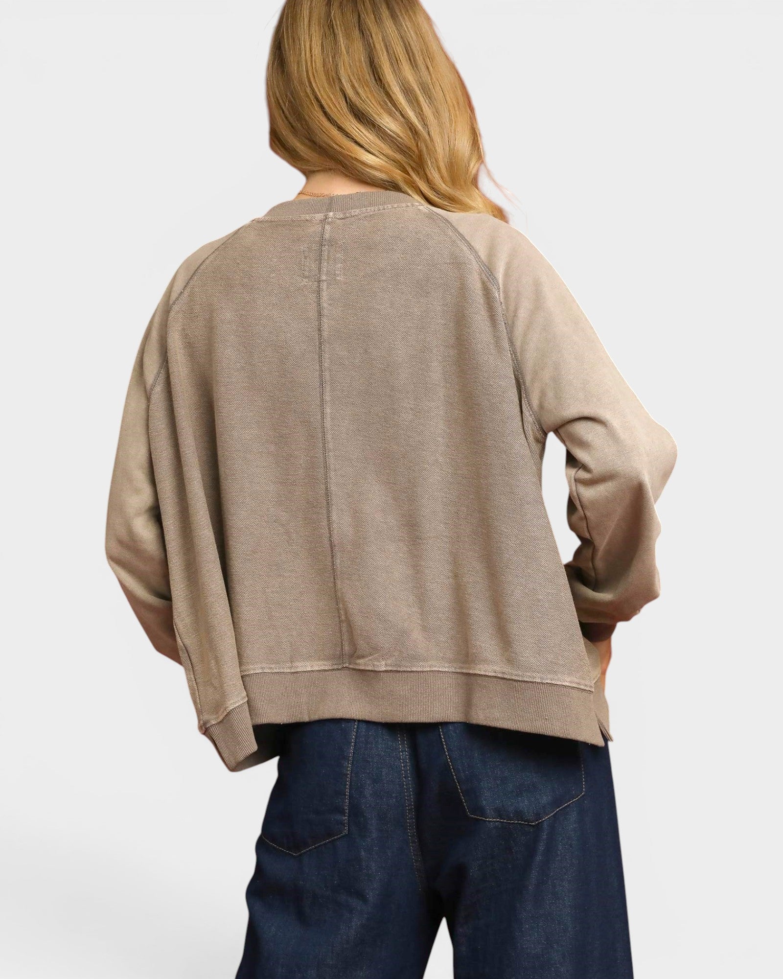 Person wearing a beige sweater and blue jeans on a white background