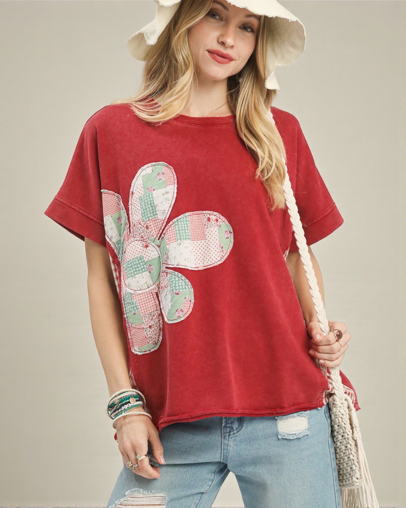 Woman wearing a red t-shirt with a flower design, holding a straw bag on a beige background