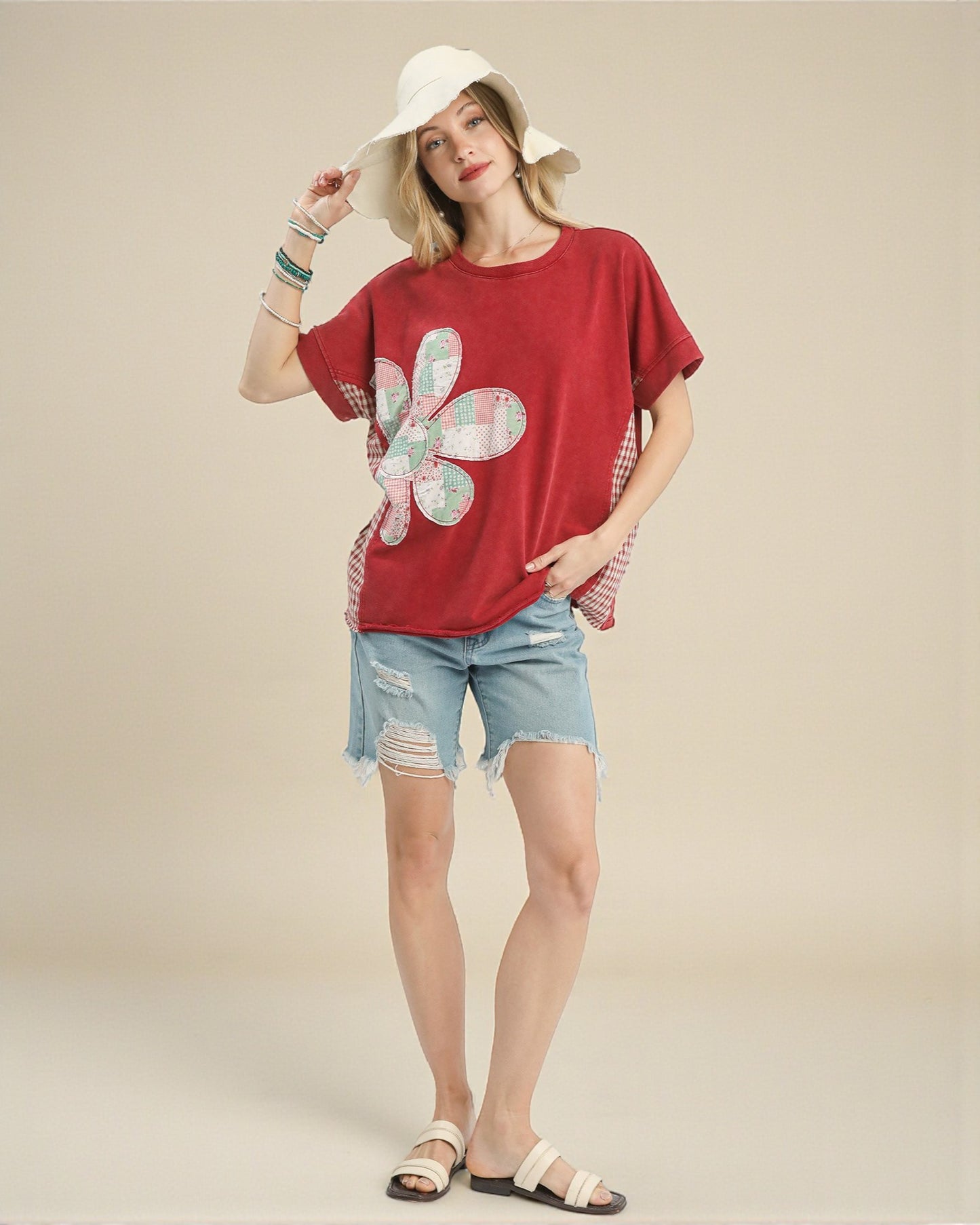 Woman wearing a red t-shirt with a floral design, denim shorts, and a white hat on a beige background