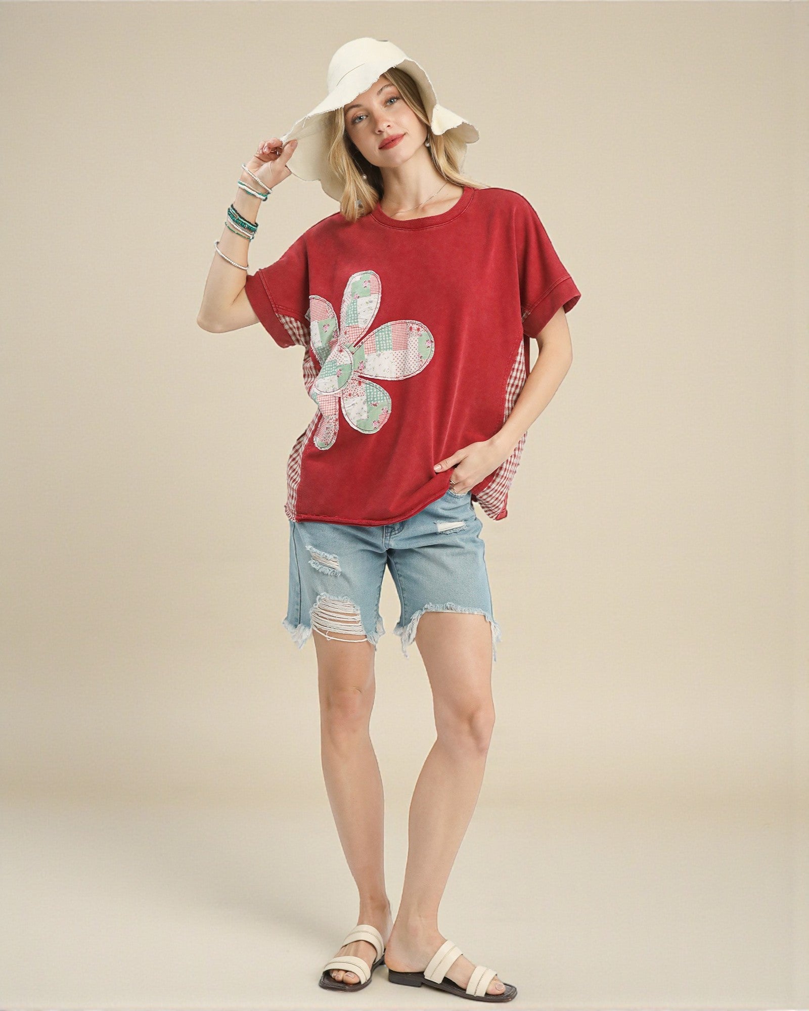 Woman wearing a red t-shirt with a floral design, denim shorts, and a white hat on a beige background