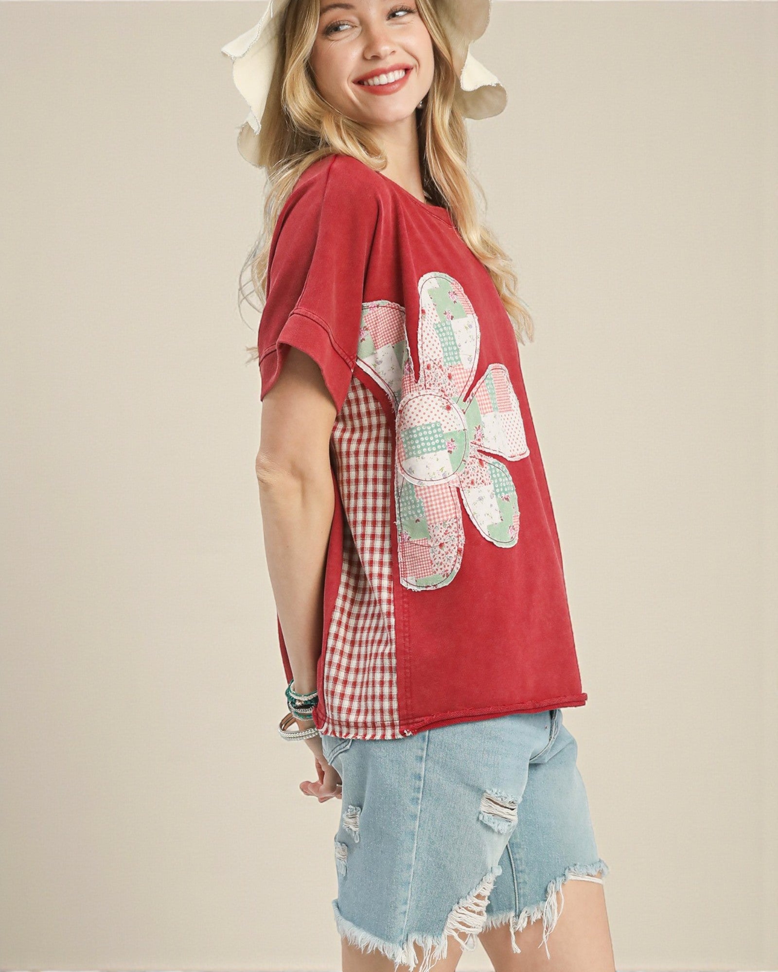 Woman wearing a red top with a floral design and denim shorts on a beige background