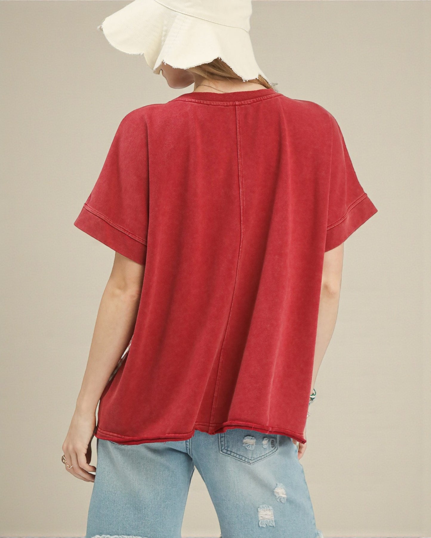 Person wearing a red t-shirt and light blue jeans with a beige background