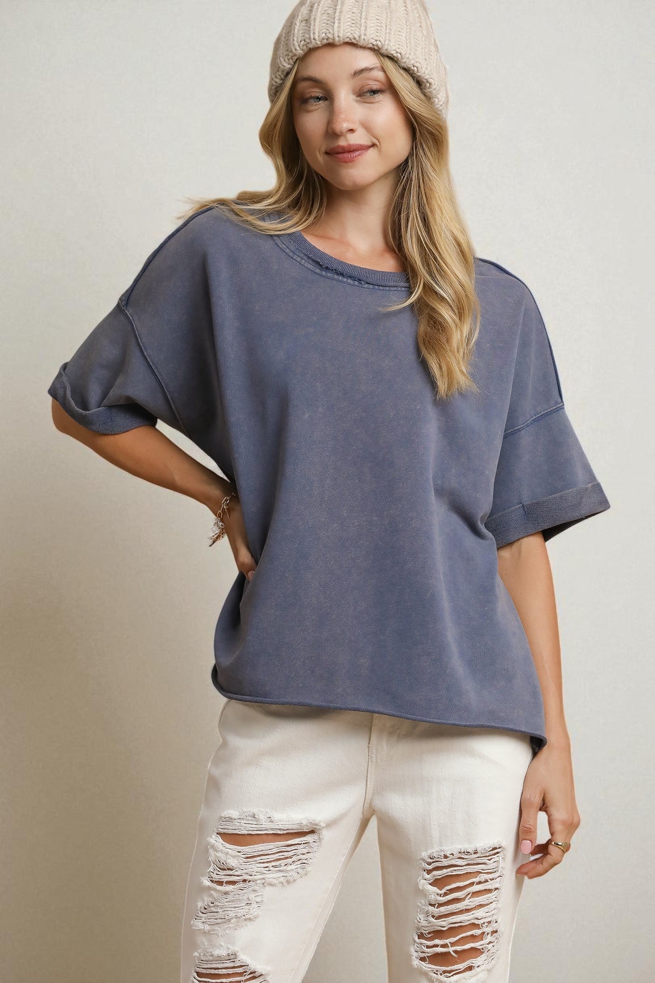 Woman wearing a blue oversized t-shirt and white distressed jeans on a plain background