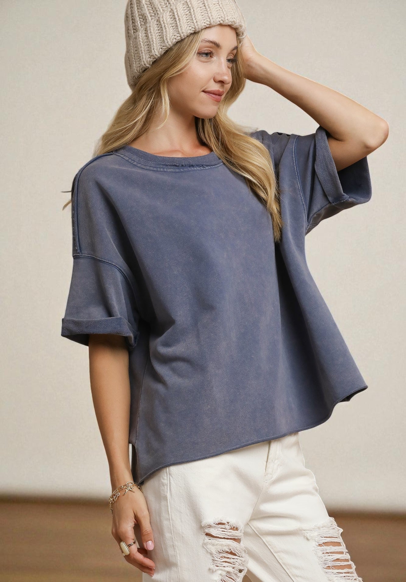 Woman wearing a blue oversized t-shirt and white pants with a beige beanie.