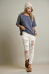 Woman wearing a blue shirt, white distressed jeans, and a beige beanie against a plain background