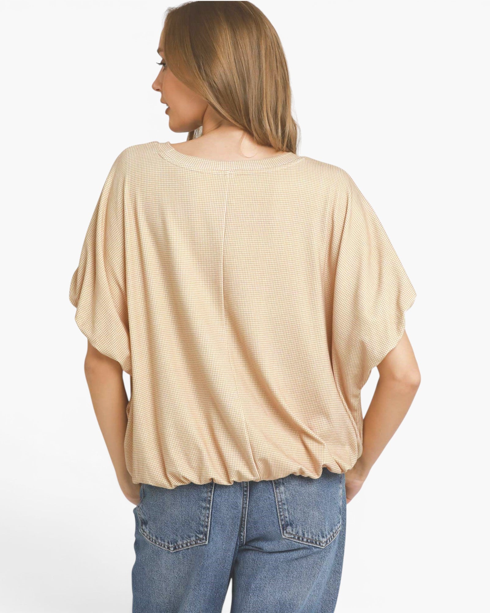 A woman shown from the back wearing a beige short-sleeve top and blue jeans against a plain white background.