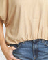 A close-up of a person wearing a beige short-sleeve top with a fine gingham-like pattern and an elasticized hem, paired with blue jeans.