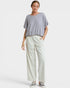 A woman modeling a loose, short-sleeve light gray top and off-white wide-leg trousers against a plain light gray studio background.