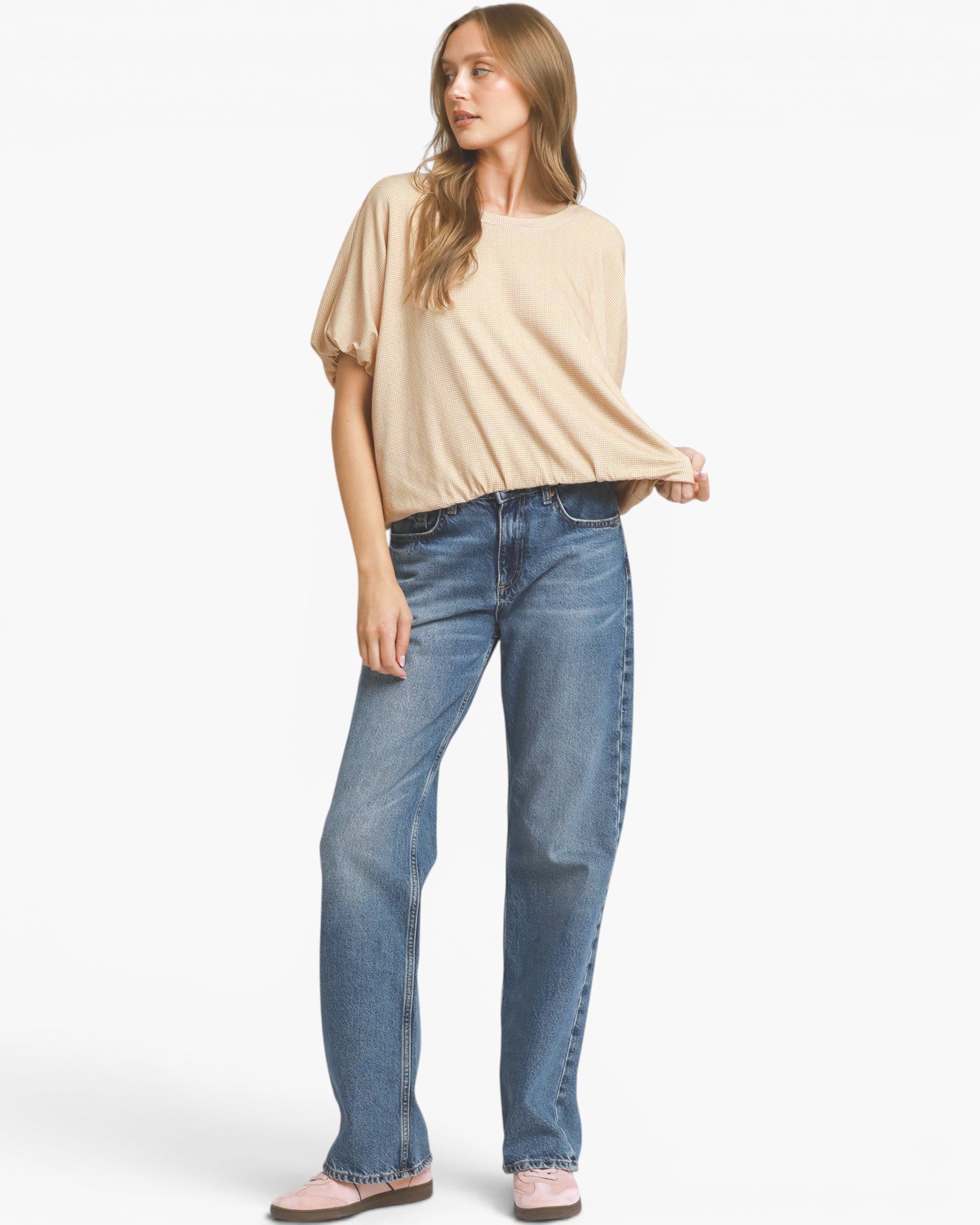 A woman modeling a beige short-sleeve top and blue jeans against a plain white studio background.