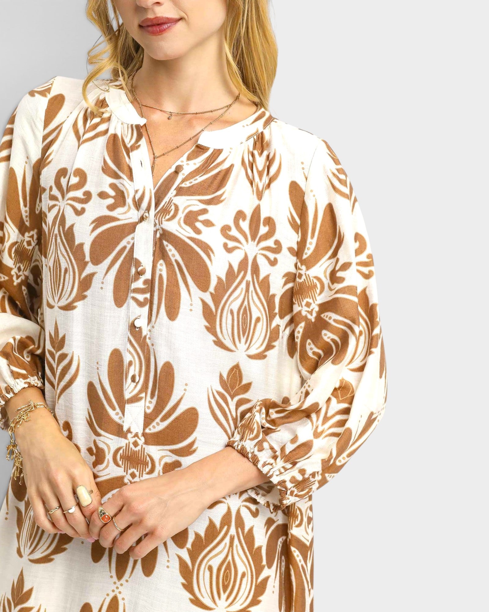 Woman wearing a brown and white patterned blouse on a plain background