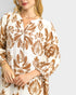 Woman wearing a brown and white patterned blouse on a plain background