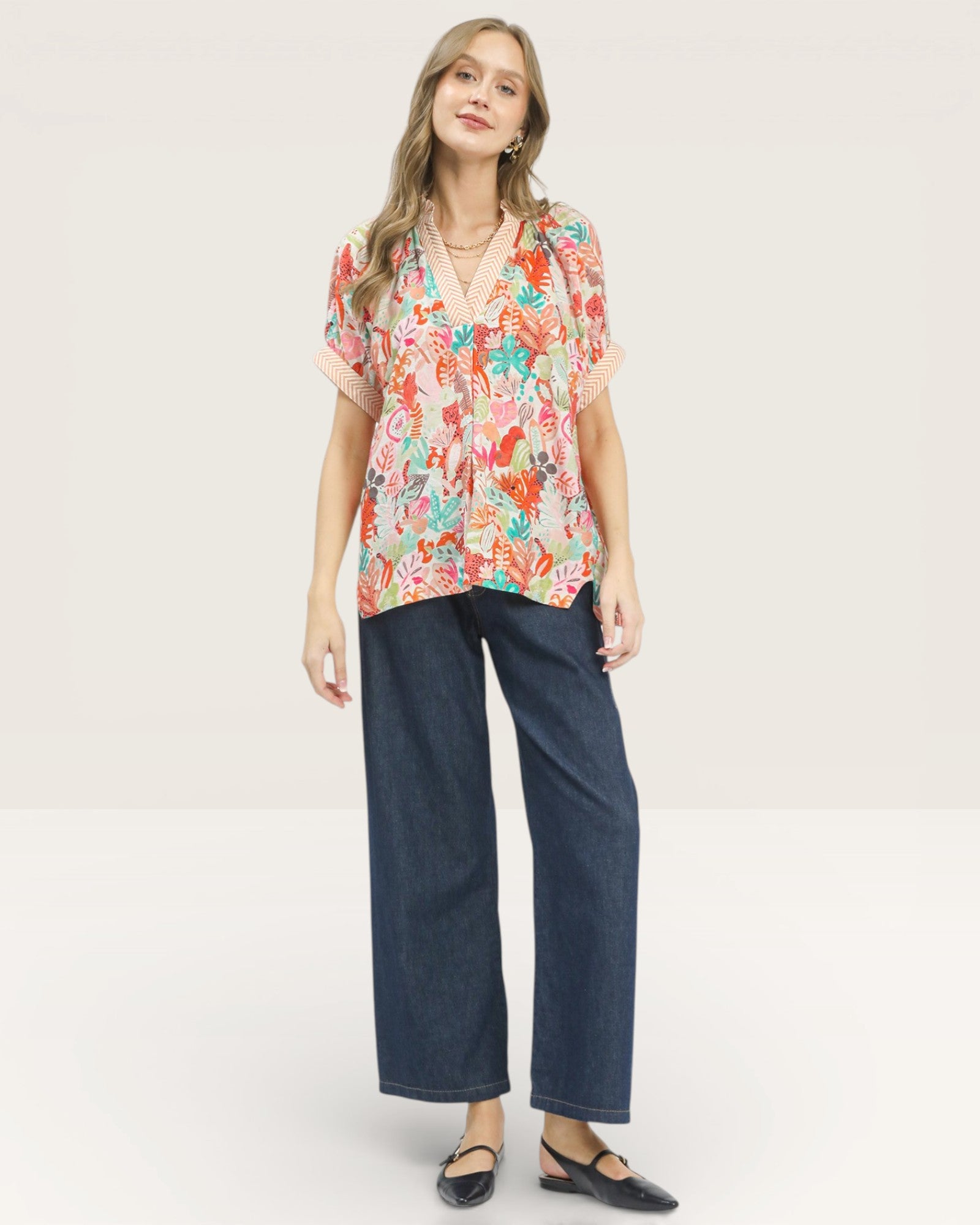 Woman wearing a colorful floral blouse and dark blue jeans on a white background