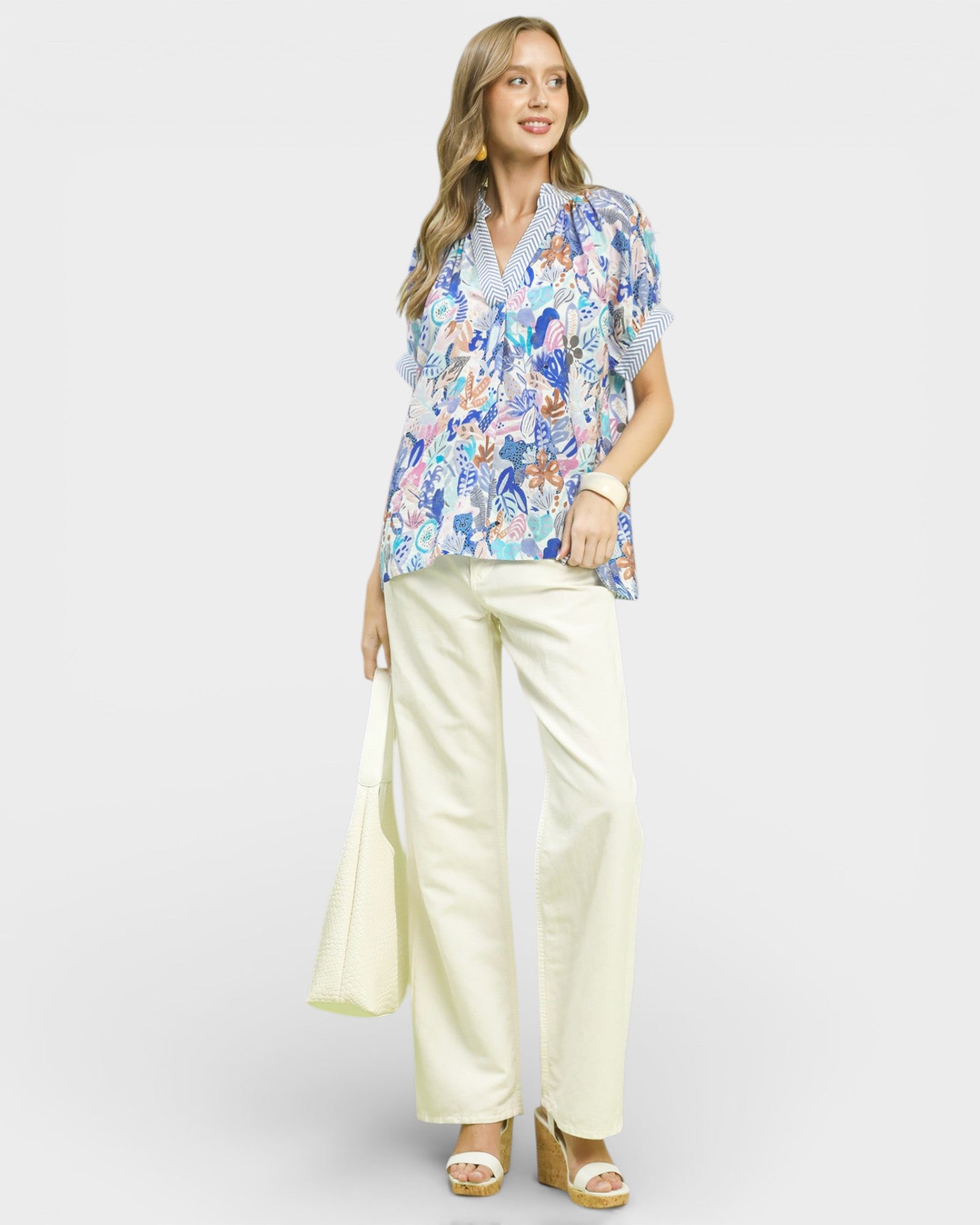 Woman wearing a floral blouse and cream pants on a white background