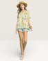 Woman wearing a floral blouse and denim shorts on a white background