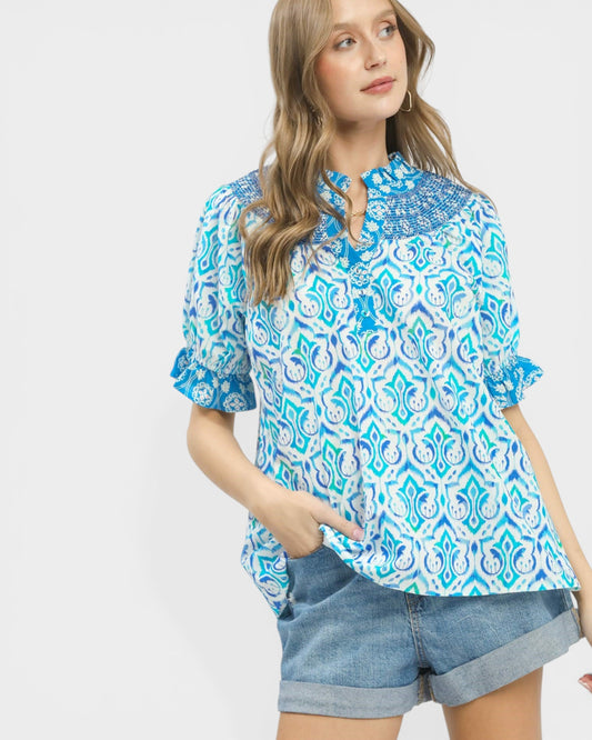 Woman wearing a blue patterned blouse and denim shorts on a white background