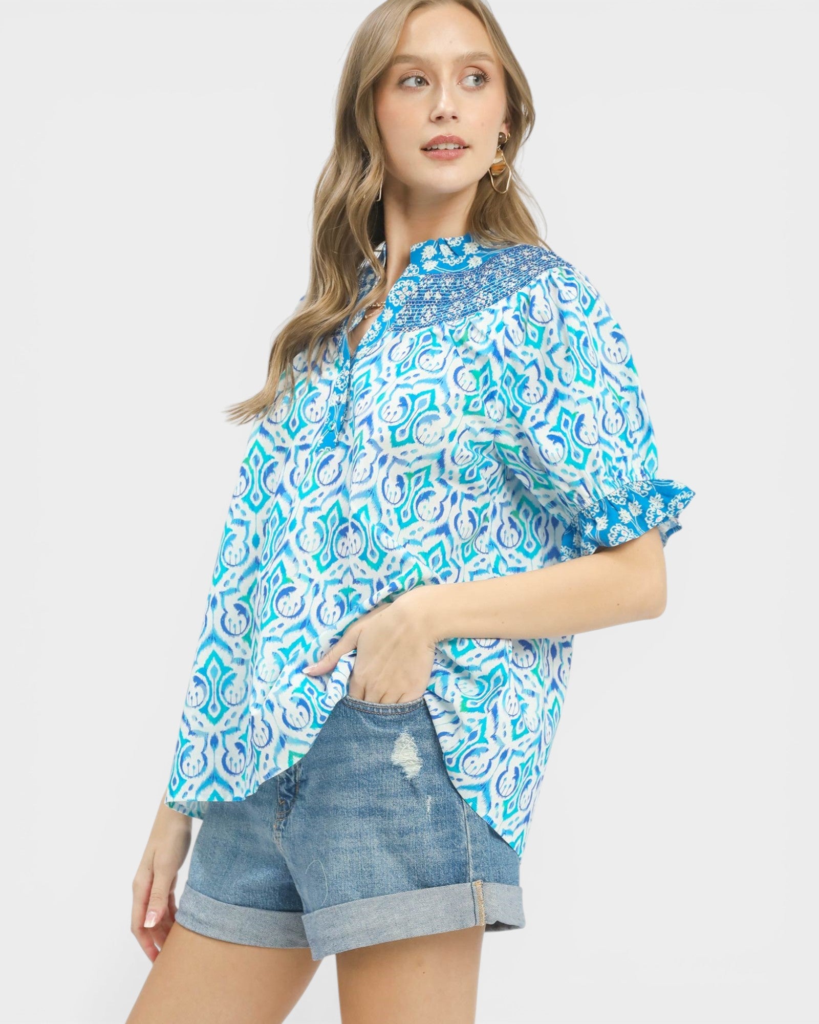 Woman wearing a blue and white patterned blouse with denim shorts on a white background