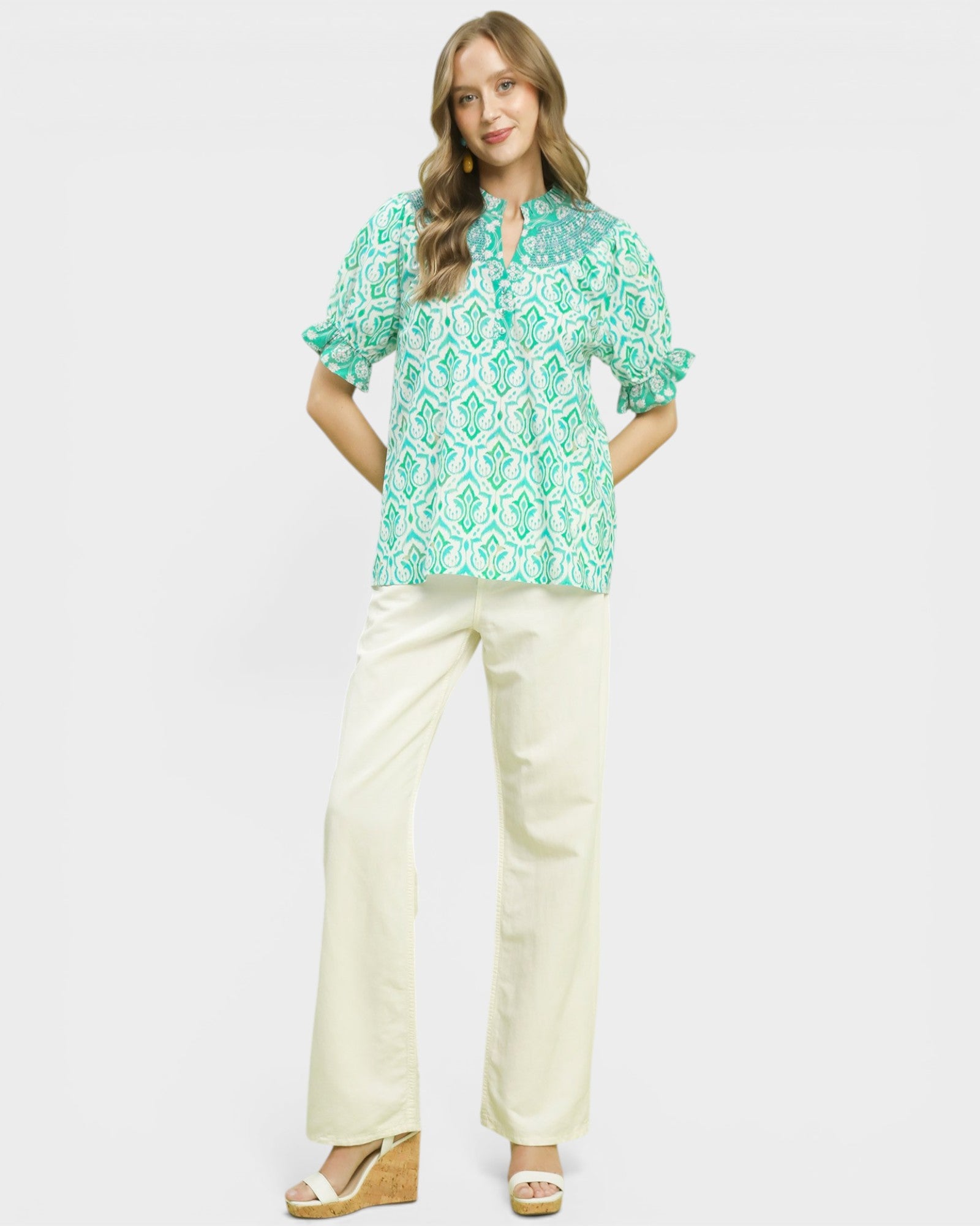 Woman wearing a green patterned top and white pants on a white background