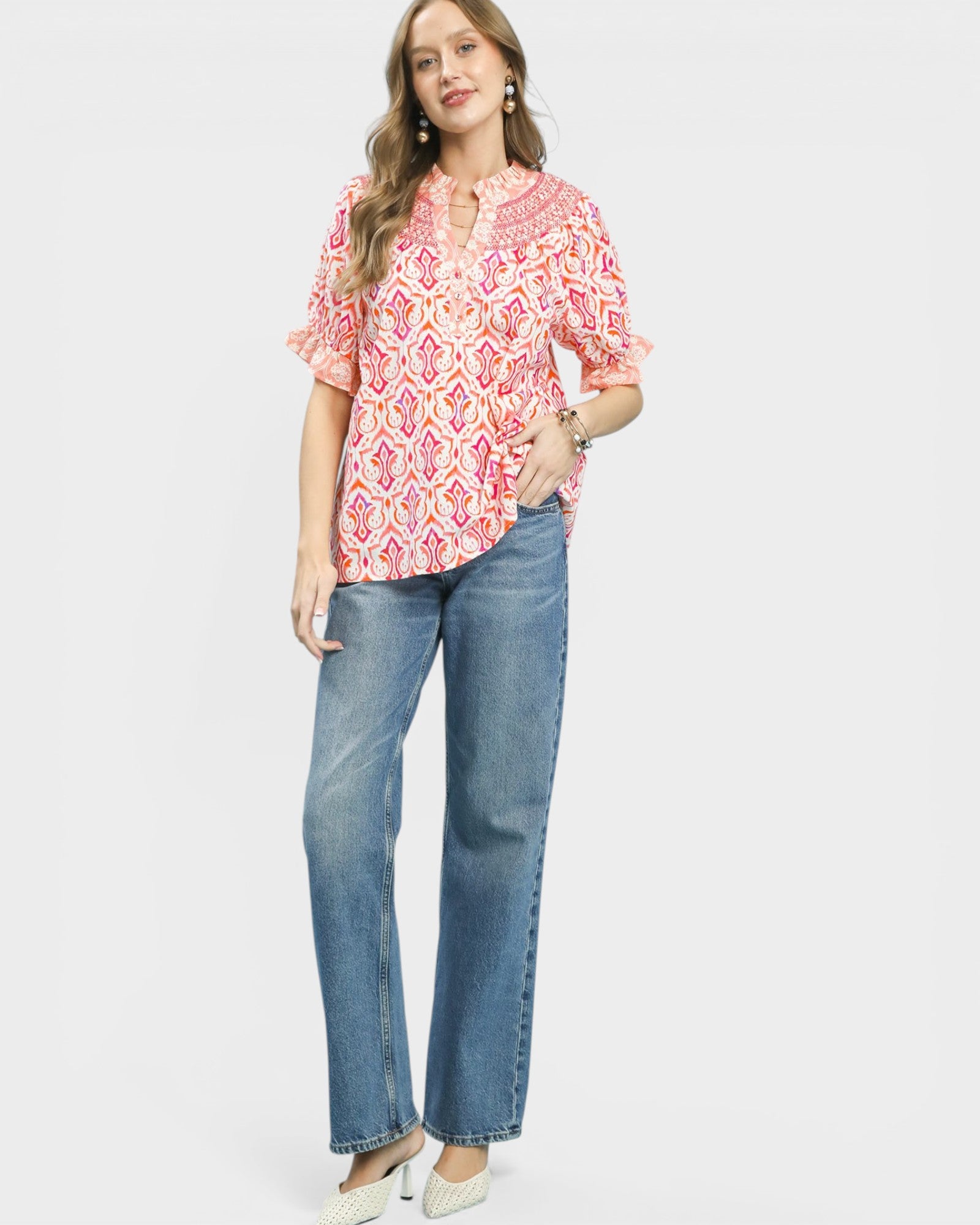 Woman wearing a pink patterned blouse and blue jeans on a white background
