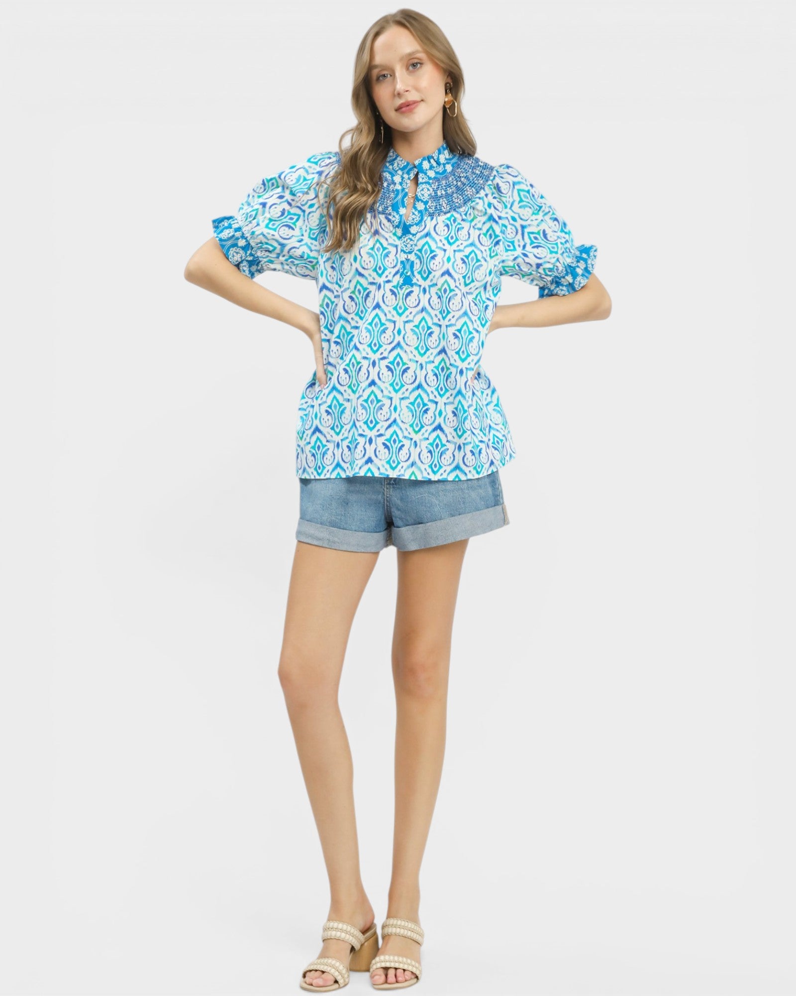 Woman wearing a blue patterned blouse and denim shorts on a white background