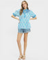 Woman wearing a blue patterned blouse and denim shorts on a white background
