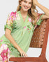 Woman wearing a green floral dress sitting on a wooden chair.