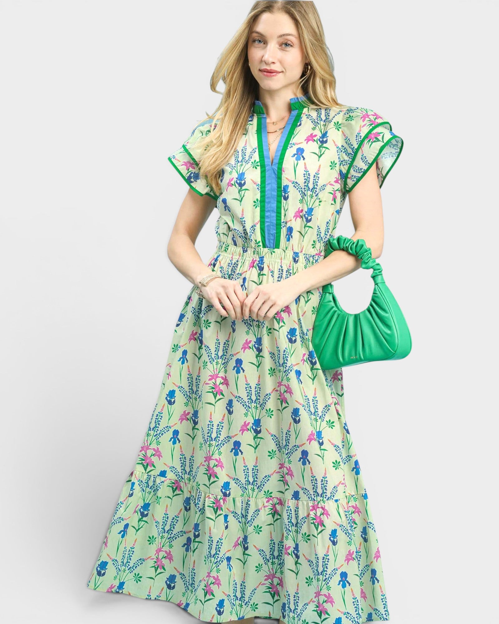 Woman wearing a floral dress holding a green handbag on a white background