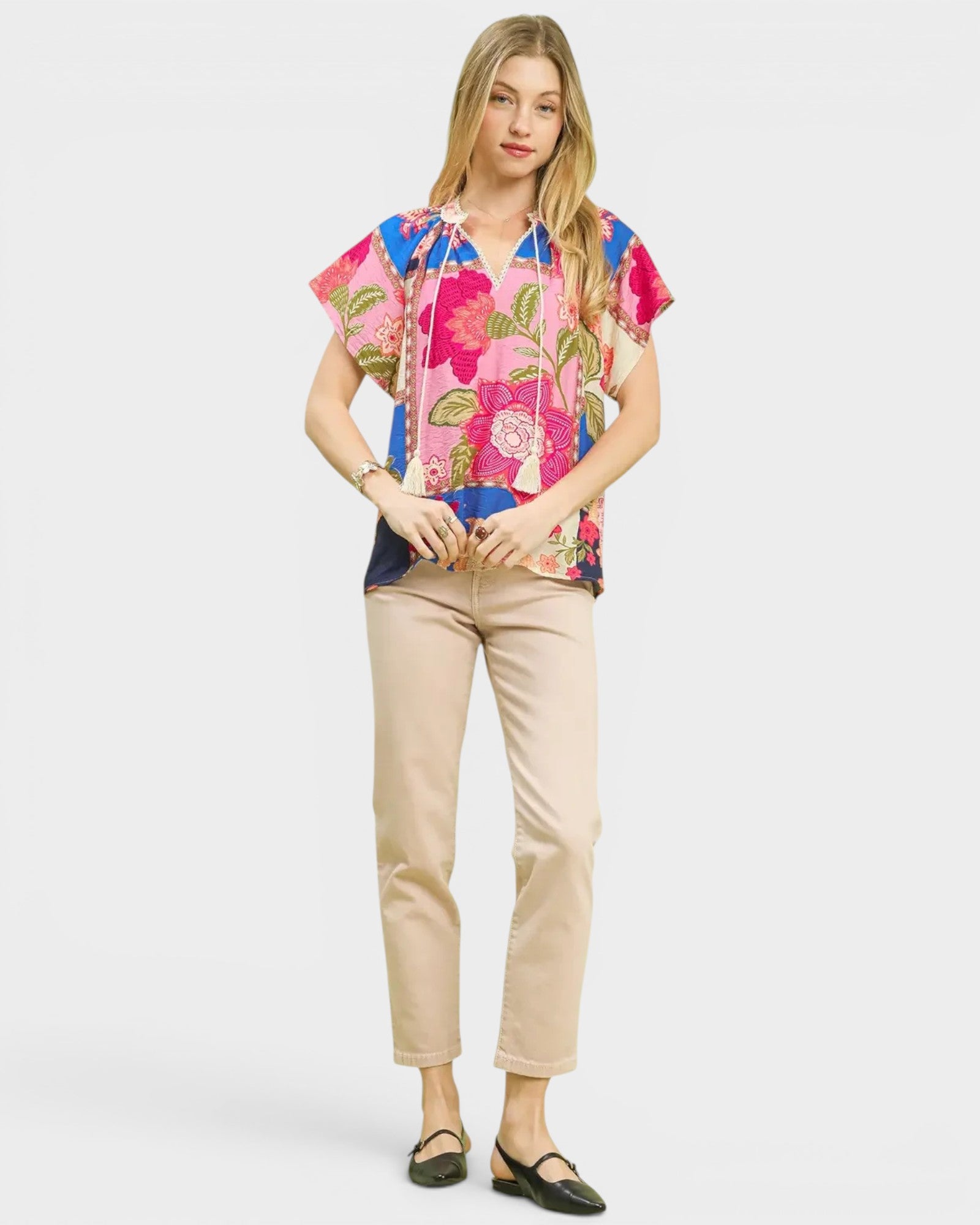 Woman wearing a colorful floral blouse and beige pants on a white background