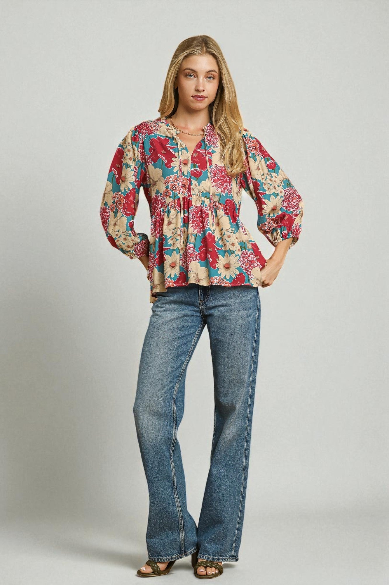 Woman wearing a floral blouse and blue jeans on a plain background
