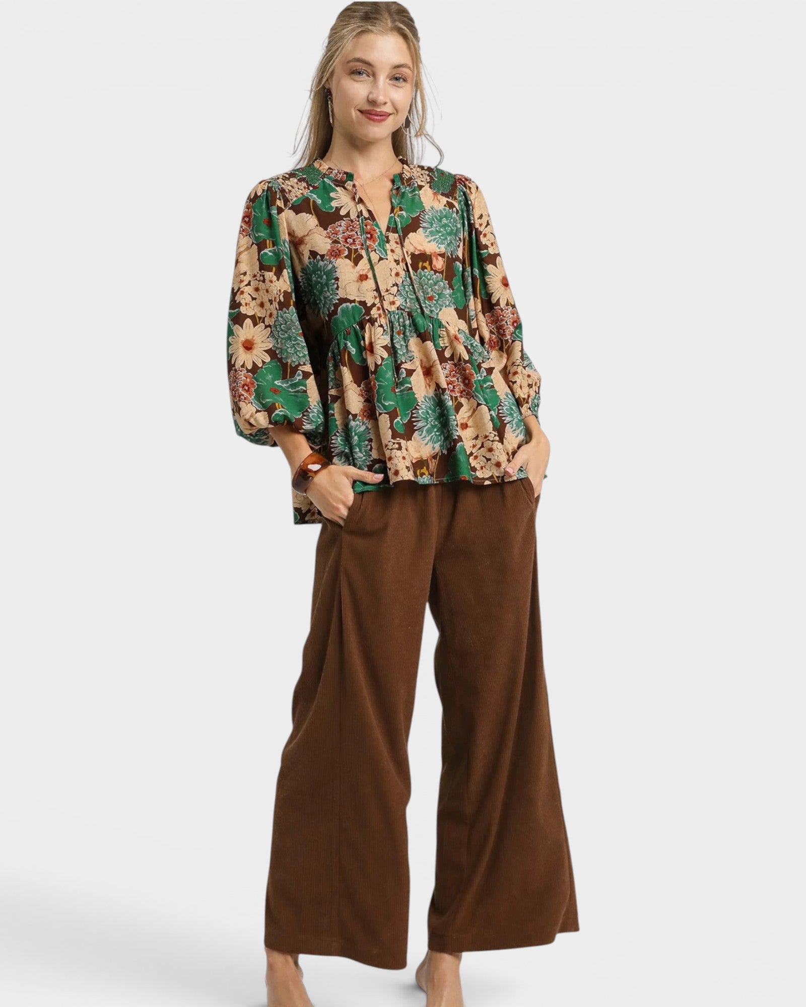 Woman wearing a patterned top and brown pants on a white background