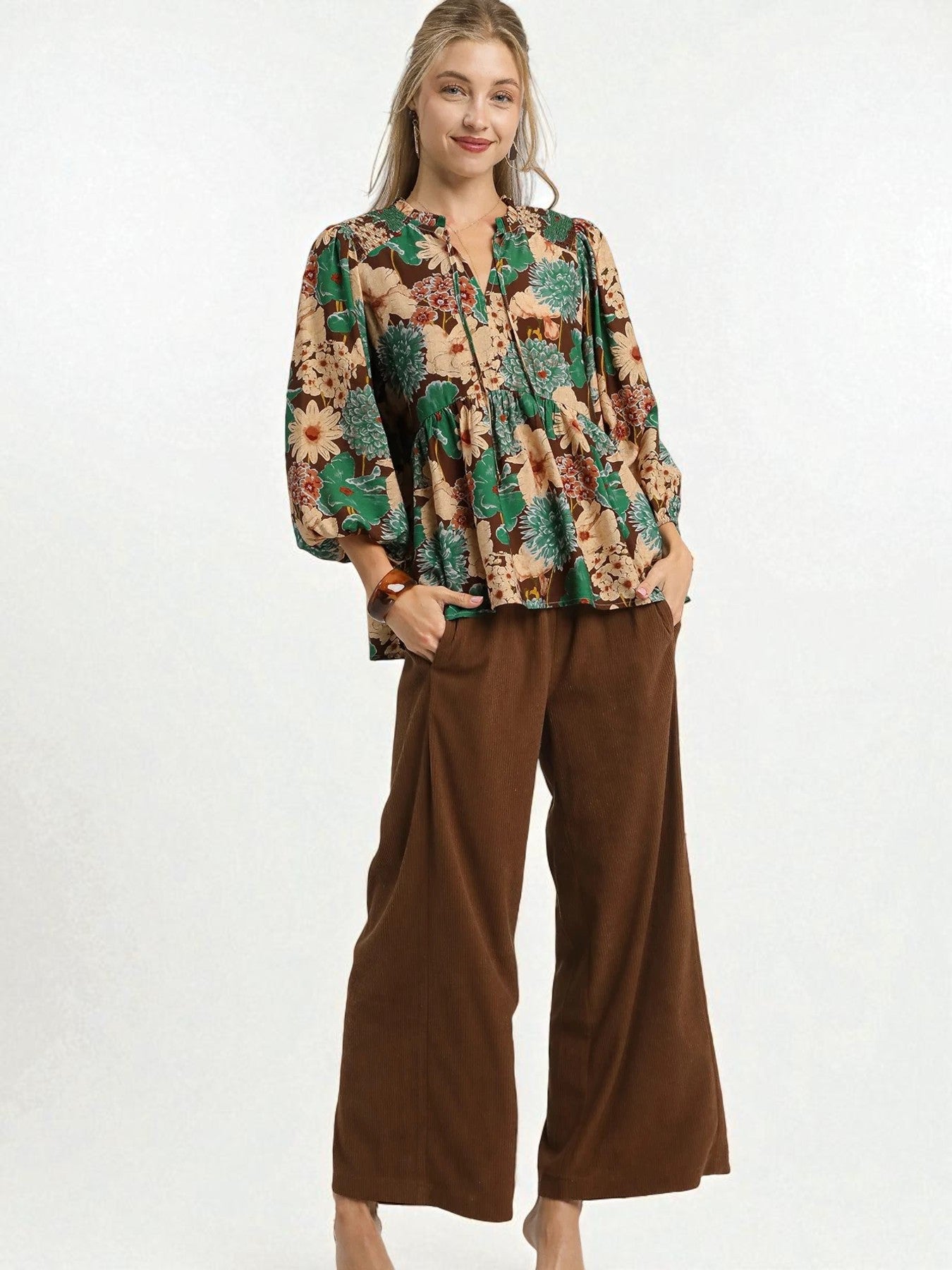 Woman wearing a patterned blouse and brown pants on a white background