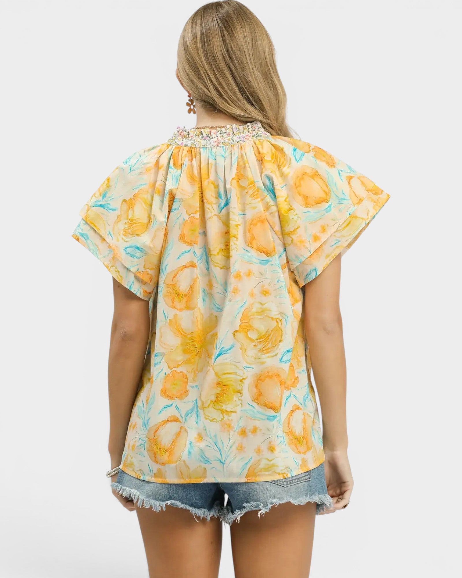 Woman wearing a yellow floral blouse with denim shorts on a white background