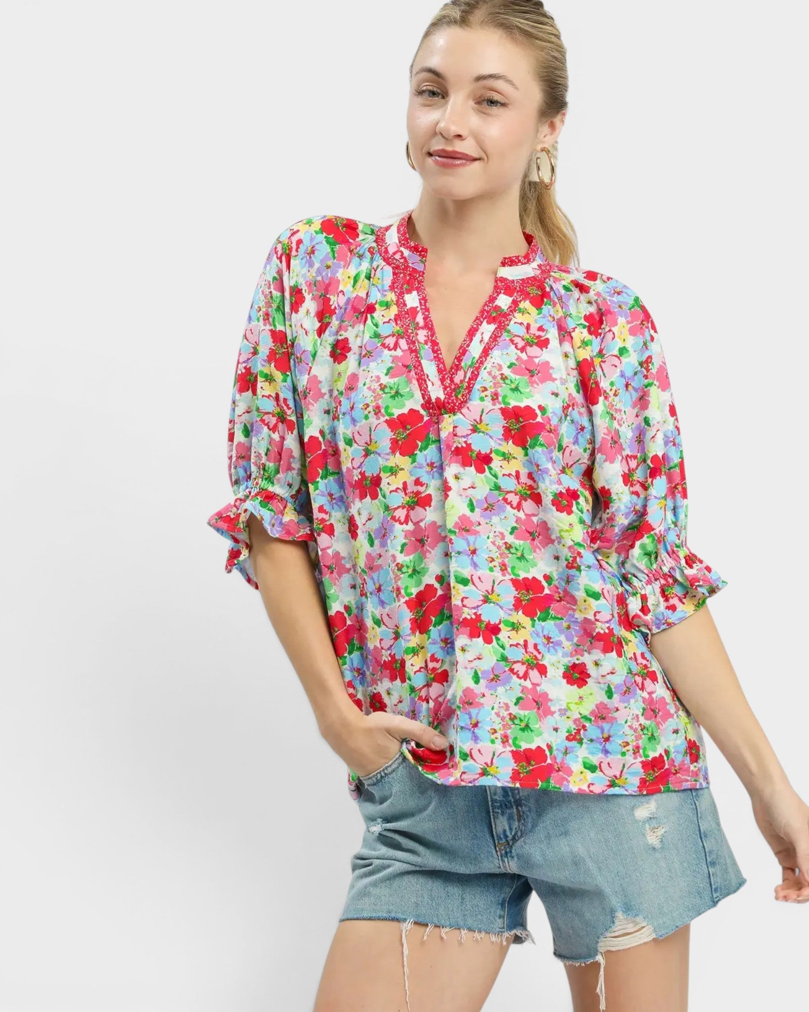 Woman wearing a colorful floral blouse and denim shorts on a white background