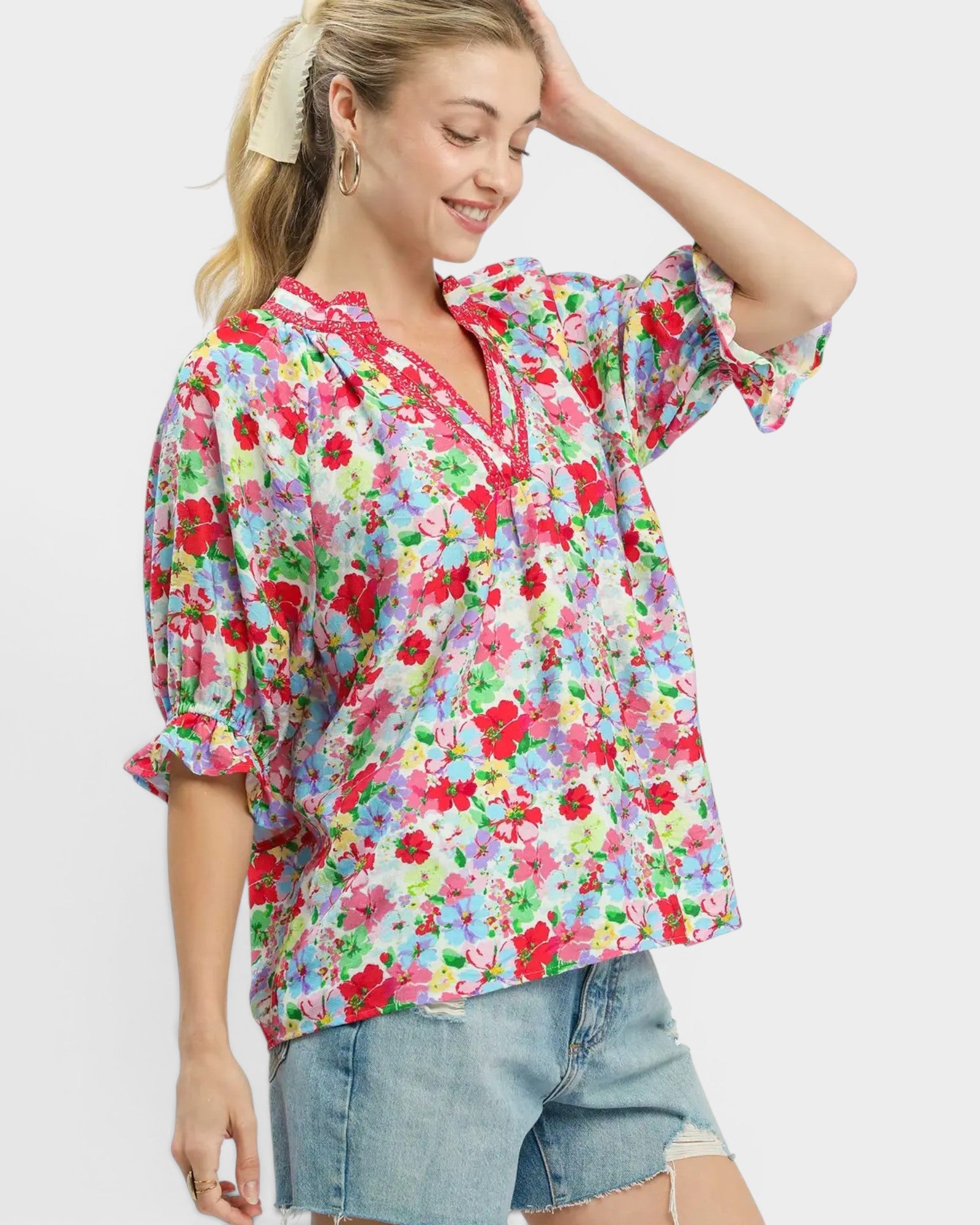 Woman wearing a colorful floral blouse and denim shorts on a white background