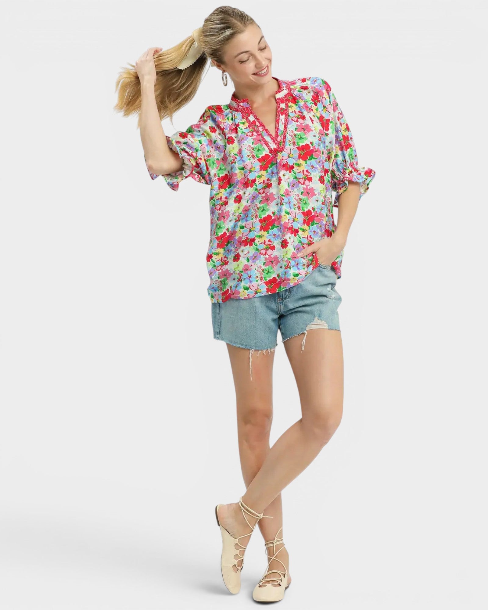 Woman wearing a colorful floral blouse and denim shorts on a white background