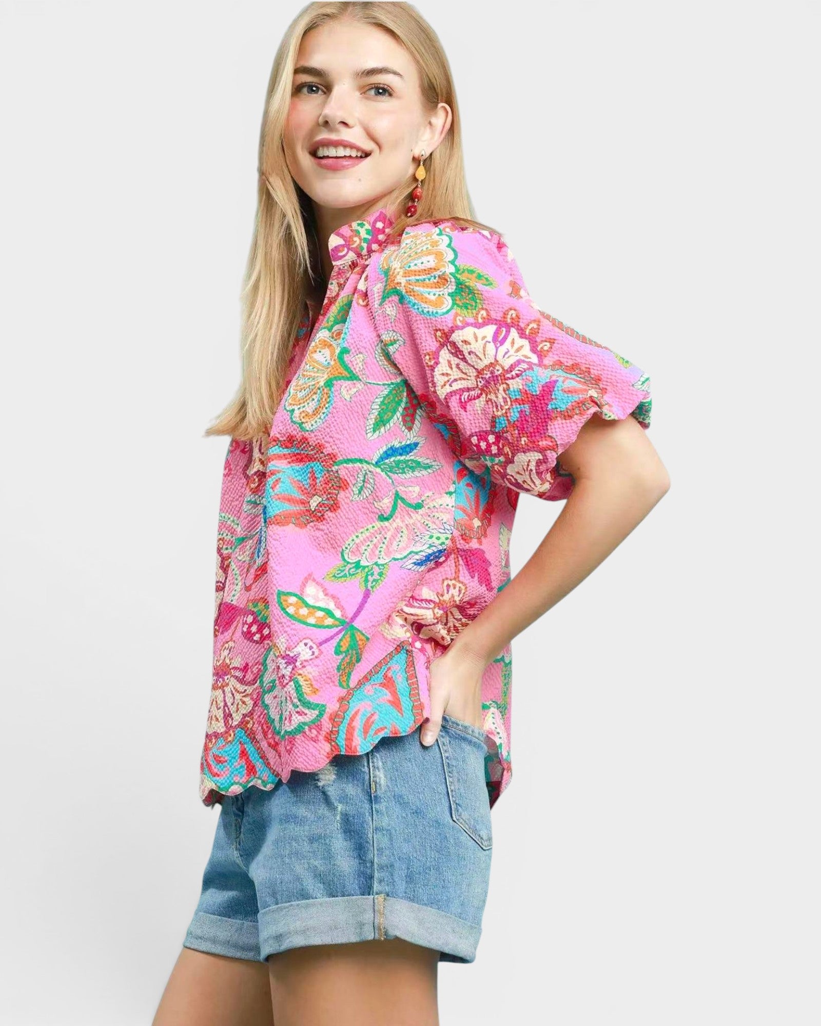 Woman wearing a colorful floral blouse and denim shorts on a white background